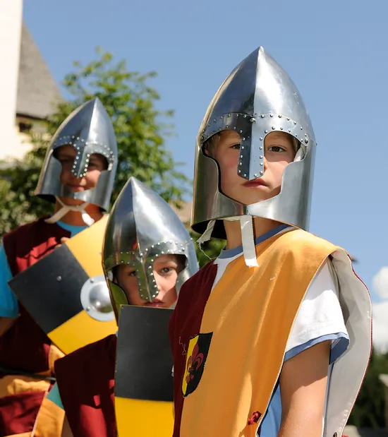 Kinder in mittelalterlichen Ritterkostümen mit Helmen und Schilden bei einer historischen Nachstellung